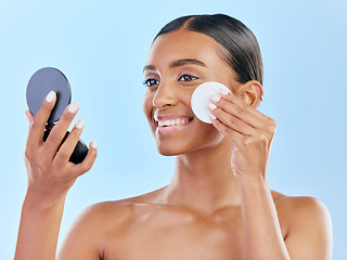 Image showing Happy woman, cotton pad and skincare with mirror for makeup removal against a blue studio background. Female person with smile for beauty cosmetics, pamper or removing foundation in facial treatment