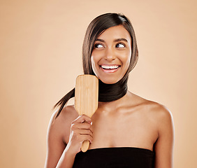 Image showing Face, smile and a woman brushing her hair in studio on a cream background for natural or luxury style. Haircare, thinking and shampoo with a young indian female model at the salon or hairdresser