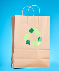 Image showing Brown paper bag, recycling sign and studio for sustainability, shopping and retail package by blue background. Eco friendly product, climate change and design for social responsibility to save planet