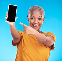 Image showing Portrait, phone screen and happy black woman point at studio advertising space, online app promo or web news. Smile, smartphone UI mockup and African person gesture at mobile deal on blue background