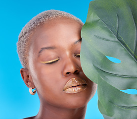 Image showing Makeup, plant and a black woman on a blue background for a wellness aesthetic. Face, beauty and an African girl or model with a leaf and organic cosmetics isolated on a studio backdrop for health