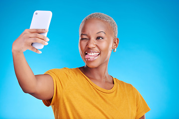 Image showing Social media, selfie and funny face with a black woman on blue background in studio to update her profile picture. Post, app and a happy young female influencer taking a photograph for her status