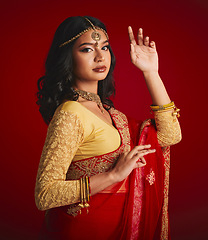 Image showing Portrait, beauty and Indian woman with fashion, traditional dress and luxury against a red studio background. Face, female person and model with cultural clothes, jewellery and gold with religion