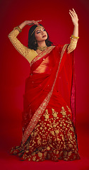 Image showing Beauty. dance and Indian woman in a traditional dress, jewellery and religion against a red studio background. Female person, girl and dancer with a cultural outfit, dancing and routine with fashion