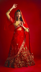 Image showing Fashion, dance and Indian woman in a traditional dress, jewellery and celebration on a red studio background. Female person, girl and model with a cultural outfit, dancing and routine with confidence