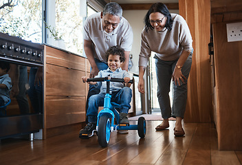 Image showing Grandparents, teaching child to ride and bike in kitchen, home or childhood memory of learning with elderly people. Kid, grandmother and grandfather with bicycle and cycling on training wheels