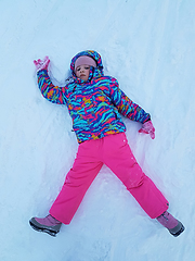 Image showing Cute little kid girl in warm ski sport suit making snow angel outdoors. Kid having fun lying on snowdrift after snow storm in winter. Children outdoor activities. Winter vacation and holidays.