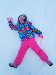 Image showing Cute little kid girl in warm ski sport suit making snow angel outdoors. Kid having fun lying on snowdrift after snow storm in winter. Children outdoor activities. Winter vacation and holidays.