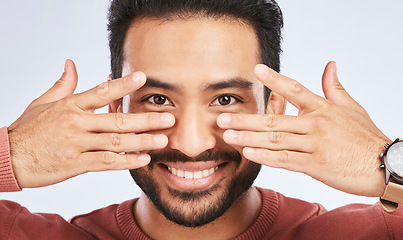 Image showing Portrait, smile and asian man with fingers on eyes in studio with confidence, personality and persona on grey background. Hands, happy and male person with hand gesture for mask, masquerade or silly