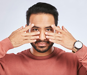 Image showing Portrait, eyes and asian man with fingers on face in studio with confidence, personality and persona on grey background. Hands, pose and male person with hand gesture for mask, masquerade or ego