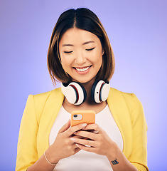 Image showing Social media, phone and happy Asian woman in studio for text message, internet meme and chat. Headphones, smile and female person on smartphone listen to audio, song and track on purple background