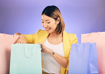 Image showing Check, shopping bag and happy woman for fashion sale, discount or retail prize on studio, purple background. Happy young model, asian person or customer with choice, giveaway and rich, wealth or gift