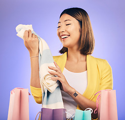 Image showing Clothes, shopping bag and happy woman with product sale, discount or promotion on a studio, purple background. Excited young model, asian person or customer fashion choice, retail and e commerce gift