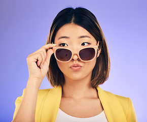 Image showing Fashion, sunglasses and a model asian woman on a purple background in studio for trendy style. Face, shades and attitude with a confident young female person looking over a stylish eyewear frame