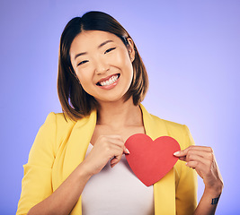 Image showing Support, asian girl and care with paper heart with portrait in purple studio or background with emotion. Woman, happy and face with love sign for peace or kindness with emoji shape for hope or smile.