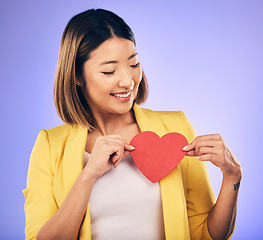 Image showing Asian girl, support and paper heart for care with smile in studio with purple background with asian. Peace, wellness and woman with love sign for kindness or hope with happiness and romance emoji.