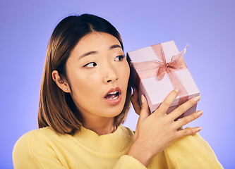 Image showing Thinking, gift and box with face of asian woman in studio for birthday, celebration and curious. Surprise, wow and party with female person and present on purple background for giveaway and package