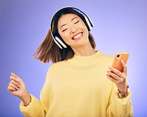 Image showing Dance, music and happy Asian woman with phone in studio for streaming, subscription and radio. Relax, headphones and female person on smartphone listen to audio, song and track on purple background