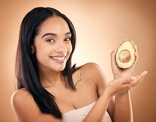 Image showing Face, smile and woman with avocado for skincare isolated on a brown background in studio. Portrait, fruit and model with food for nutrition, skin health and vegan diet, vitamin c or natural cosmetics