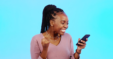 Image showing Black woman, smartphone and fist for celebration, lucky winner and achievement against a blue studio background. African American female, happy lady and cellphone with email, social media and victory