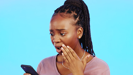 Image showing Phone, wow and surprise with a black woman in studio on a blue background looking shocked at news. Mobile, social media or shock and a female indoor with an omg or wtf hand gesture over her mouth