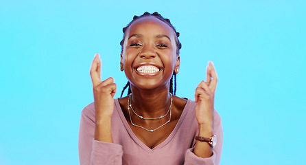 Image showing Face, fingers crossed and black woman with smile, hope and motivation with lady against blue studio background. Portrait, African American female and girl with gesture for luck, wish and emoji sign