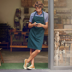 Image showing Coffee shop, typing and phone of a man as a small business owner at front door. Entrepreneur person as barista, manager or waiter in restaurant with mobile app for service, marketing or communication