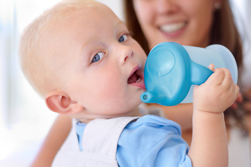 Image showing Portrait, family and a baby boy drinking water from a bottle with his mother in the blurred background. Face, kids and hydration with a young child in his home for a drink during child development