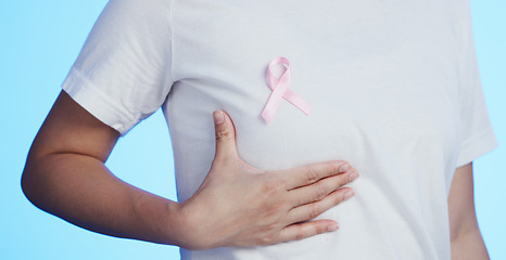 Image showing Pink ribbon, breast cancer and awareness with a woman in studio on a blue background for health. Chest, medical and healthcare with a female placing a bow, symbol or sign of recognition in october