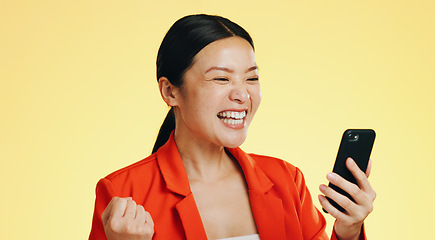 Image showing Winner, success celebration and Asian woman with phone in studio isolated on a yellow background. Surprise, fist pump or happy female with mobile to celebrate after winning lottery prize or good news