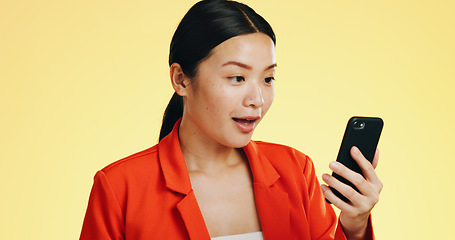 Image showing Winner, success celebration and Asian woman with phone in studio isolated on a yellow background. Surprise, fist pump or happy female with mobile to celebrate after winning lottery prize or good news