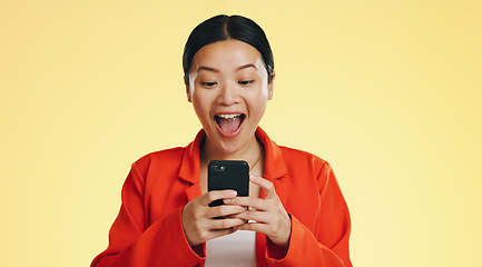 Image showing Winner, success celebration and Asian woman with phone in studio isolated on a yellow background. Surprise, fist pump or happy female with mobile to celebrate after winning lottery prize or good news