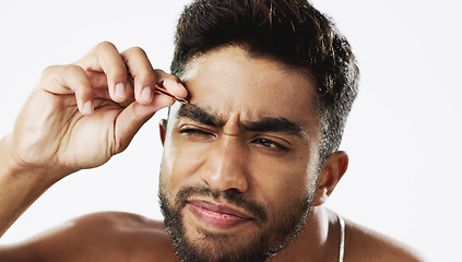 Image showing Man grooming his eyebrows with a tweezer in studio for self care, beauty and cleanliness. Hair removal, tweezing and male model from India doing facial epilation plucking routine by white background.