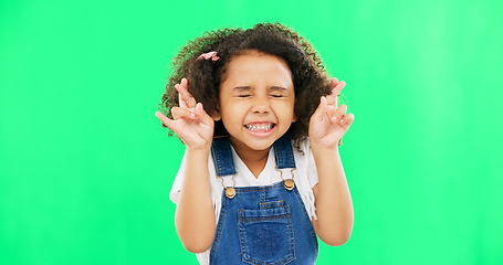 Image showing Fingers crossed, wish and praying with girl in studio for good luck, hope and optimism. Excited, emoji and closed eyes with child isolated on green background for miracle, positive and youth