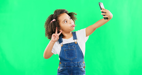 Image showing Silly little girl, selfie and peace sign on green screen with goofy facial expressions against a studio background. Female child or kid making funny face with hand sign for photo or vlog on mockup