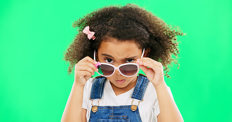 Image showing Child, portrait and sunglasses with an attitude on green screen background peeking over glasses. Black girl kid in studio for comic, funny and facial expression or mood while angry or curious