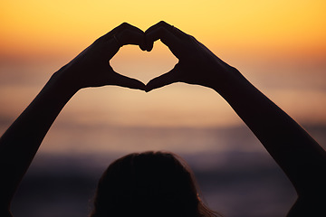 Image showing Woman, heart hand and shadow at sunset at beach and ocean with peace and zen hands sign. Silhouette, nature and sea on a vacation with calm meditation and love emoji gesture outdoor at sunrise