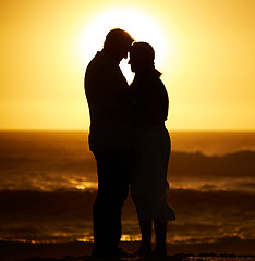 Image showing Silhouette, couple and love on a beach at sunset for vacation or holiday outdoor. Romantic man and woman hug in nature with creative sky, space and ocean for care, shadow art and travel or freedom