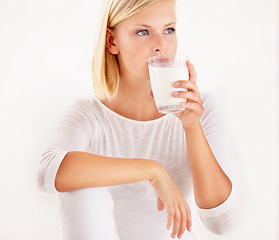 Image showing Thinking, milk and calcium with a woman drinking from a glass in studio isolated on a white background. Diet, nutrition and detox with a healthy young female enjoying a drink for vitamins or minerals