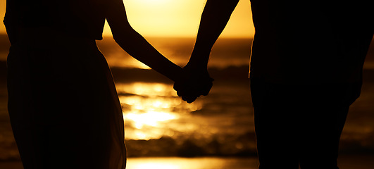 Image showing Silhouette, couple and holding hands at sunset on beach for vacation or holiday outdoor. Behind man and woman in nature with creative art, space and ocean for love, shadow and travel or freedom