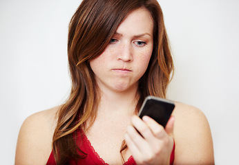 Image showing Phone, text message and an angry woman in studio on a white background unhappy while reading bad news. Social media, internet and app with a young female looking upset while checking her mobile inbox