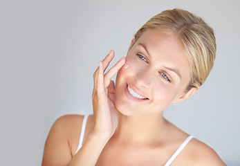 Image showing Smile, skincare and woman with cream, cosmetics and dermatology against a grey studio background. Female person, model or girl with lotion, touching face and pamper treatment with grooming and beauty