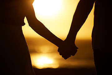 Image showing Holding hands, couple and silhouette on beach at sunset for vacation or holiday outdoor. Behind man and woman in nature with peace, calm and ocean for love, creative shadow and travel or freedom