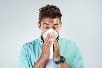 Image showing Sick, tissue and face of man blowing nose in studio with flu, illness and virus on white background. Health, wellness and male person with handkerchief for hay fever, cold and sneeze for allergy