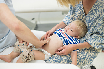 Image showing Infant baby boy child being examined by his pediatrician doctor during a standard medical checkup in presence and comfort of his mother. National public health and childs care care koncept.