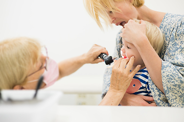 Image showing Infant baby boy child being examined by his pediatrician doctor during a standard medical checkup in presence and comfort of his mother. National public health and childs care care koncept.