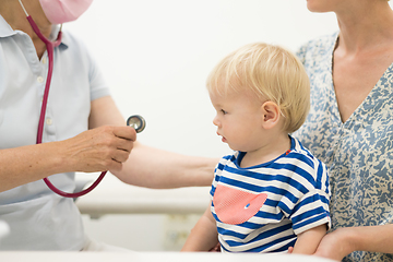 Image showing Infant baby boy child being examined by his pediatrician doctor during a standard medical checkup in presence and comfort of his mother. National public health and childs care care koncept.