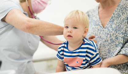 Image showing Infant baby boy child being examined by his pediatrician doctor during a standard medical checkup in presence and comfort of his mother. National public health and childs care care koncept.