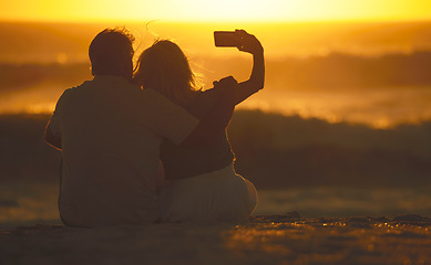 Image showing Travel, couple and selfie at sunset on a beach for vacation or holiday outdoor. Behind romantic man and woman in nature with peace, calm and ocean for quality time, love and freedom or photo memory