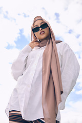 Image showing Portrait, fashion and a muslim woman outdoor on a blue sky background in sunglasses and scarf for contemporary style. Islam, faith and hijab with a trendy young arab person outside in modern clothing